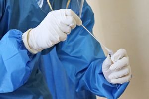 Healthcare worker in PPE performing a COVID-19 swab test in a medical setting.